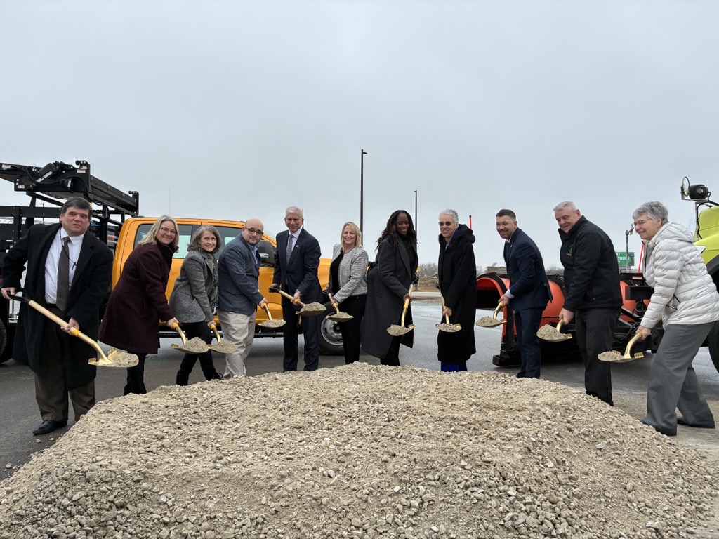 Several people stand around a large pile of gravel with shovels in their hands to signify the groundbreaking of the Touhy Avenue project.