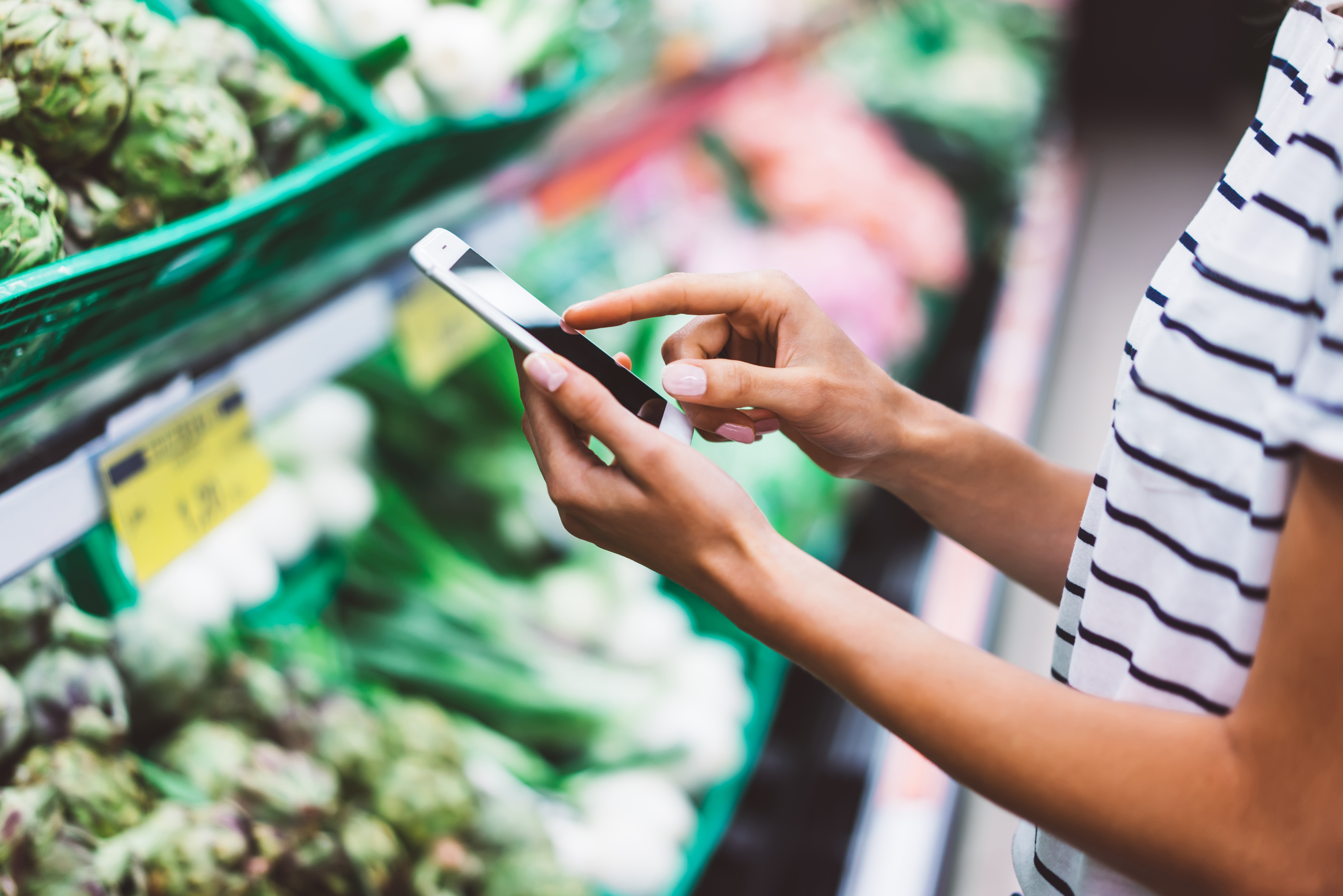 A shopper within a grocery store checking their phone in the produce section.