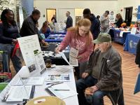 A resource fair vendor shows paperwork to a veteran in attendance.